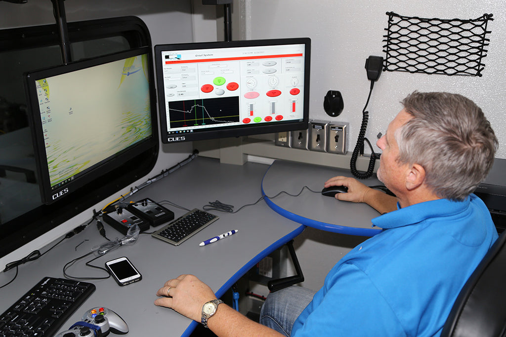 Operator at a CUES control room desk with a monitor showing grout system software