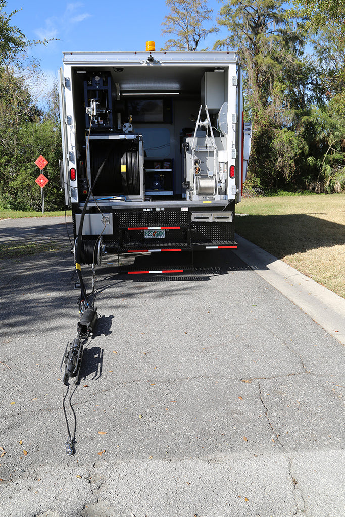 Rear of a CUES grout truck with doors open, reels inside and a cable-mounted unit on the pavement